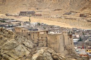 Stone buildings on a rocky hills with small village in the background.