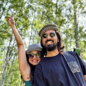 A man and woman are posing for a photo in the woods