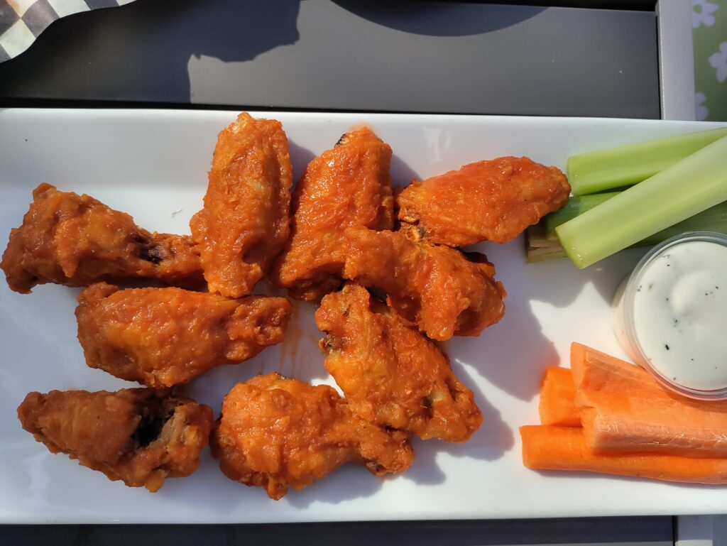 A plate with chicken wings, carrots, celery and dip.