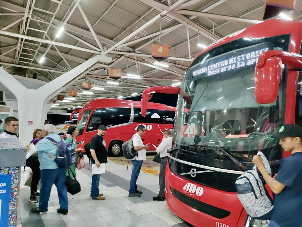 A group of people standing in a large building with red buses