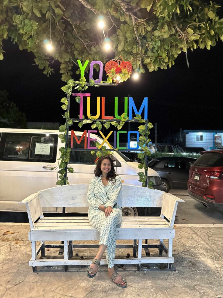 A person sitting in on a bench in front of I love Tulum sign in background