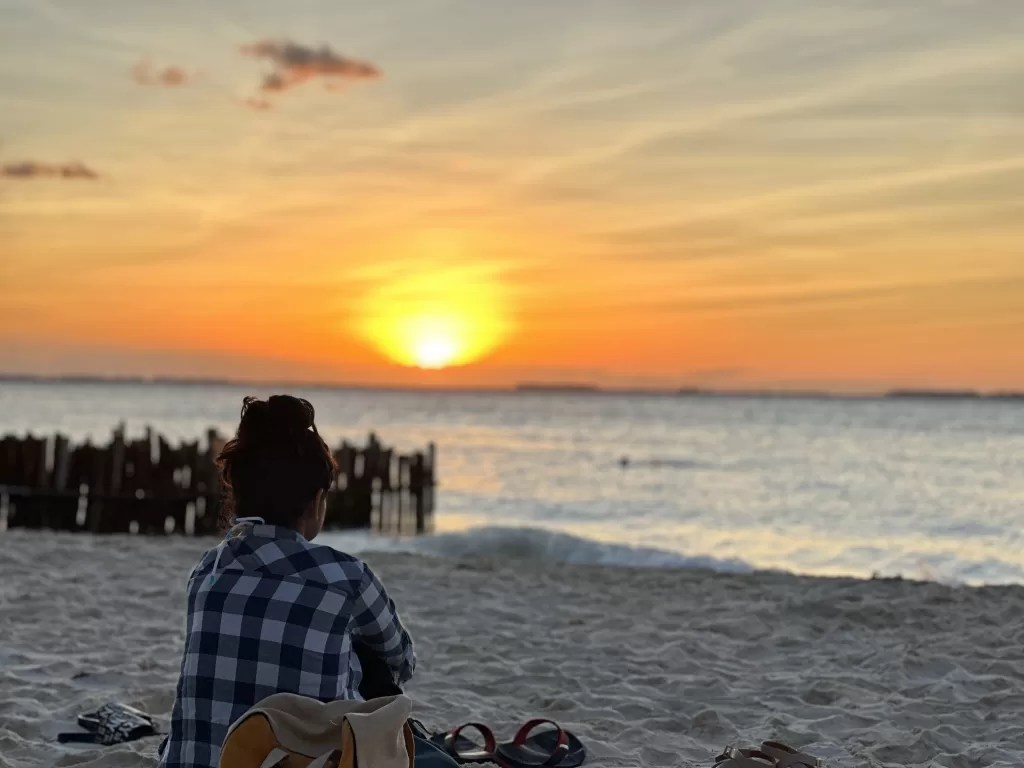 A person looking at the sunset and sitting on the beach.