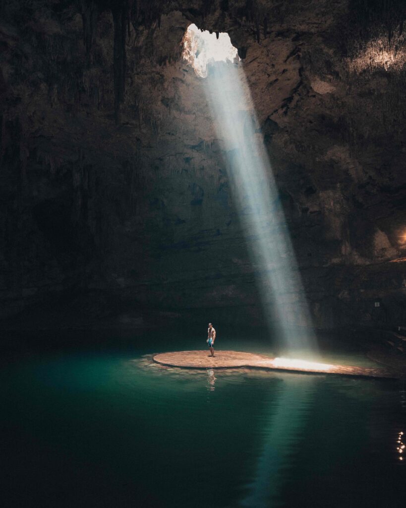 A person standing in a cave with a light coming from the ceiling