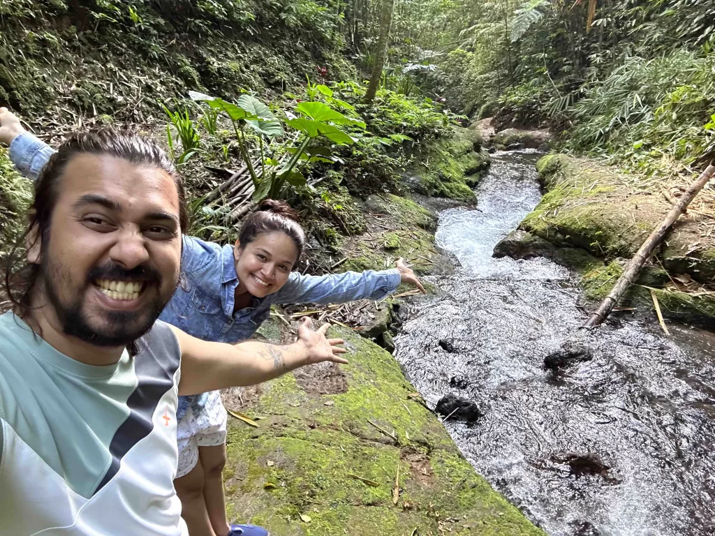 A person and a person posing with a stream and rocks behind.