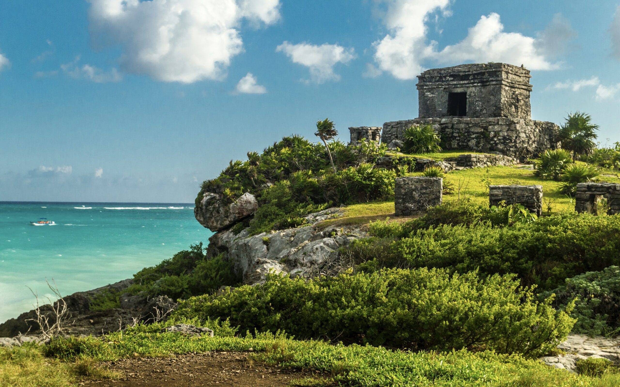 a stone building on a hill by the ocean with Tulum in the background