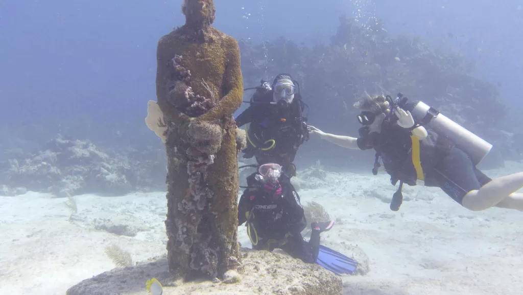 Scuba divers next to a statue underwater