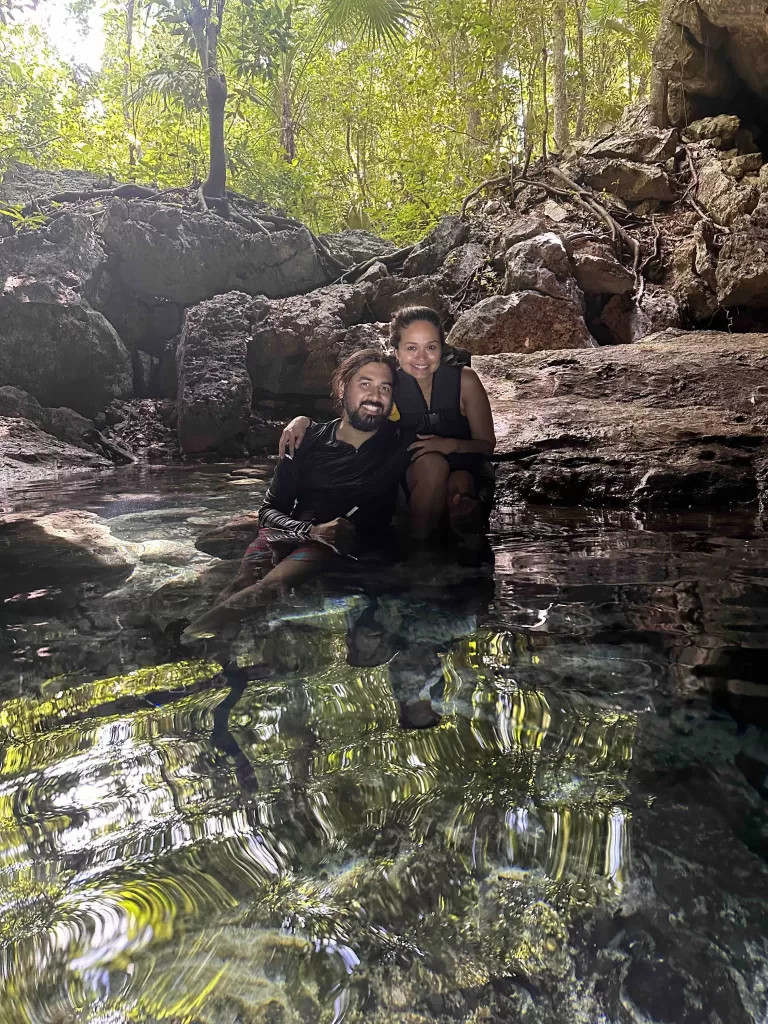 A person and a person posing sitting on rocks near water.