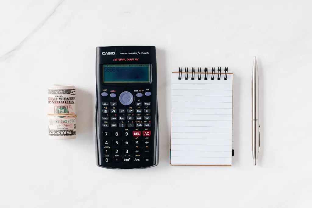 a calculator and notepad next to a pen and paper money