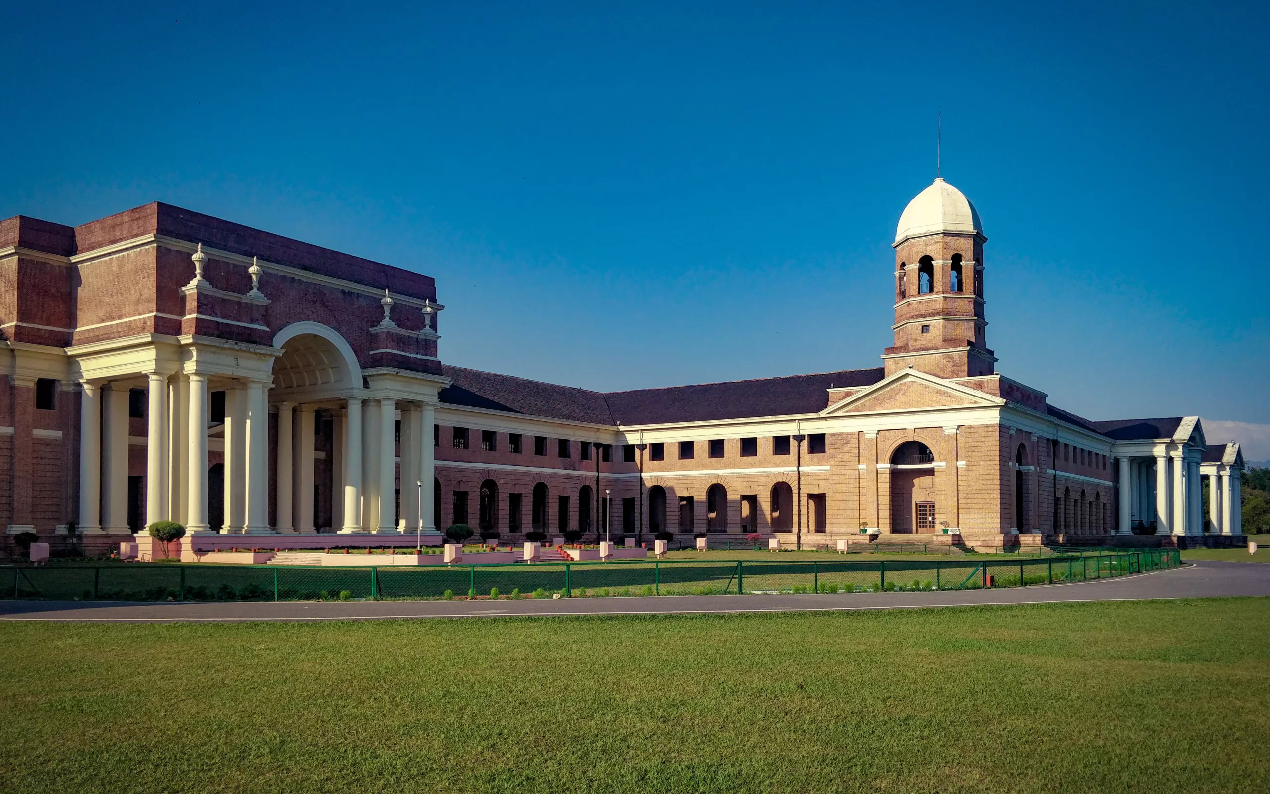 A large brick building with a lawn and a building with a tower