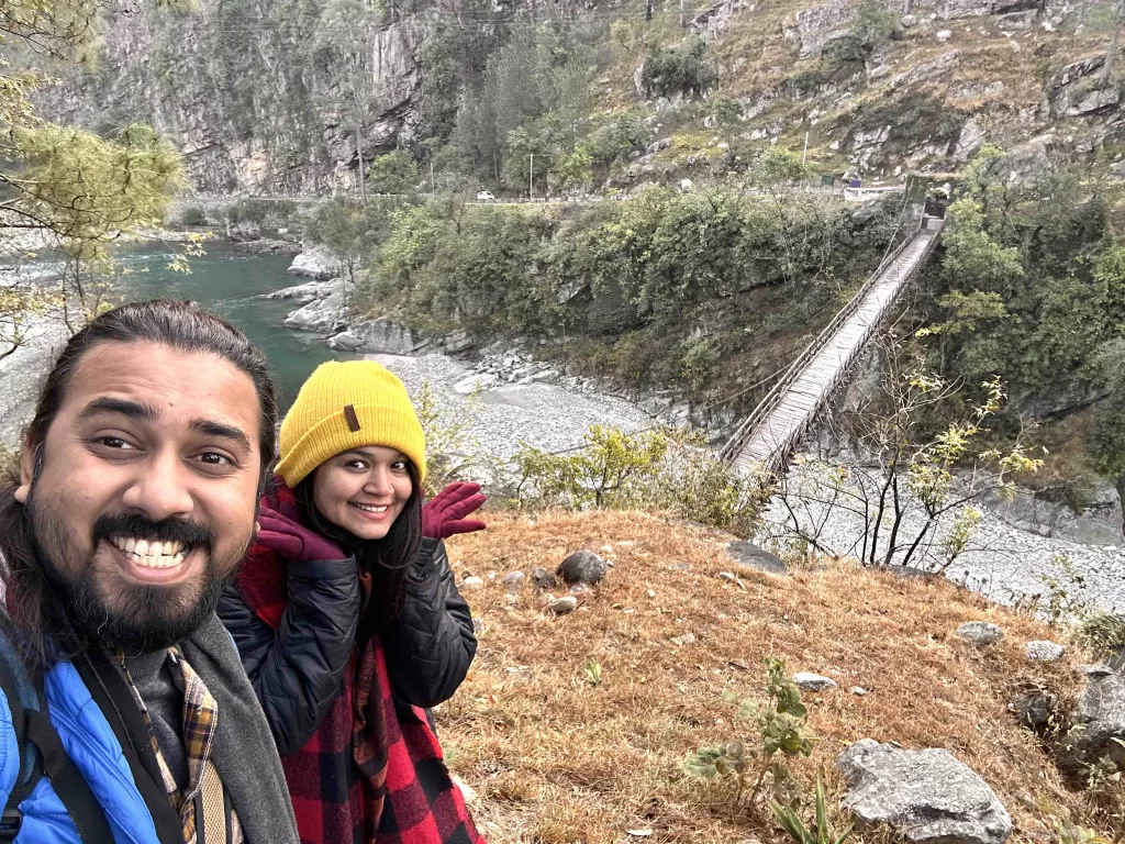 A person and a person posing in front of a bridge and ravine.