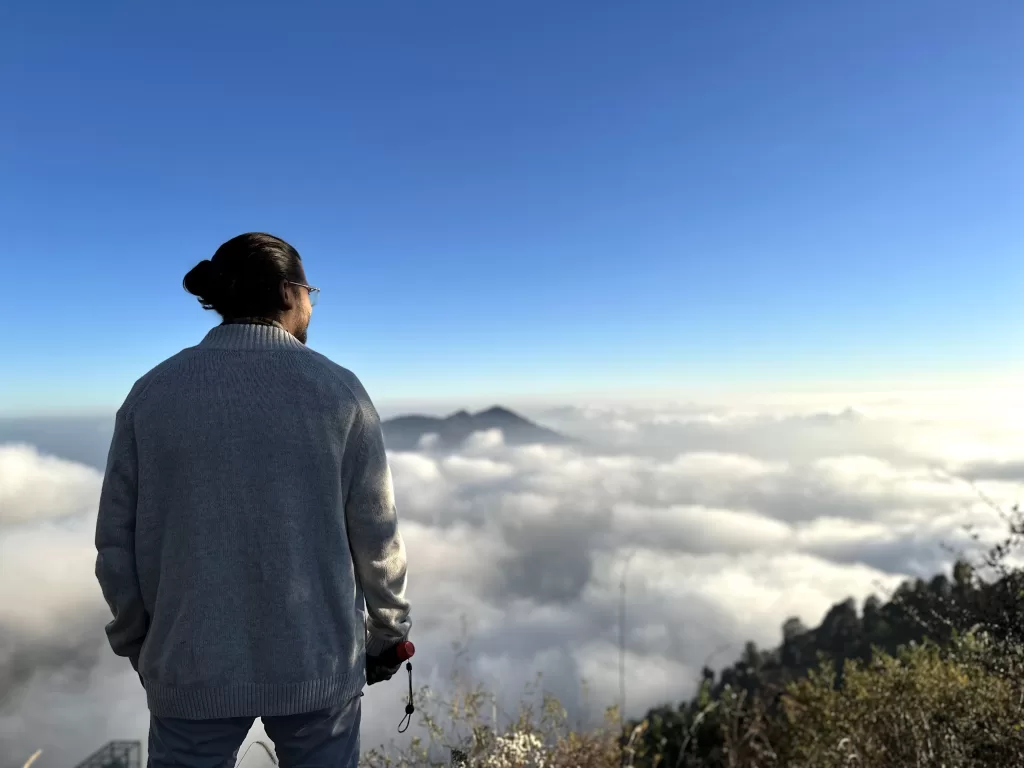 A person standing on a mountain looking at clouds. Dhanaulti, one of the places to visit near Dehradun