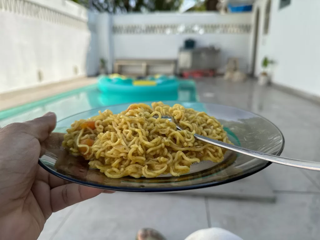 A hand holding a plate of noodles