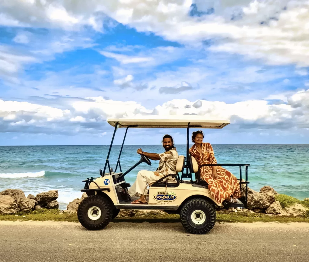 A girl and boy in a golf cart with blue sea in the background