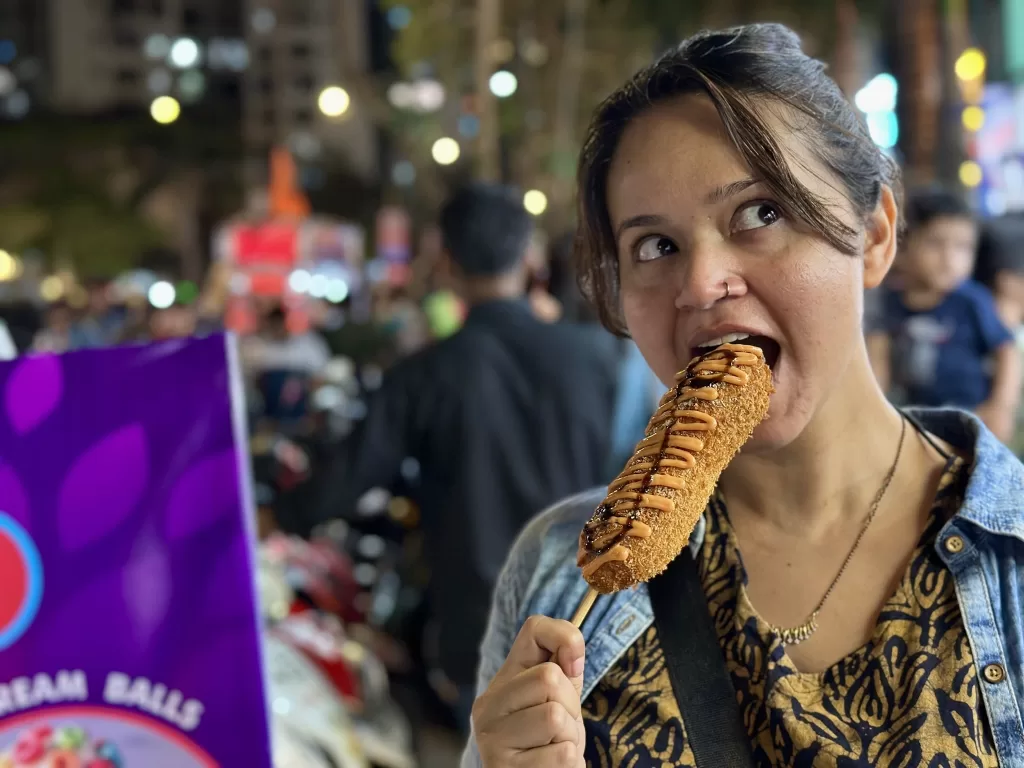 A person eating a corn dog. Amazing food at Mahavir Nagar Khau Gali