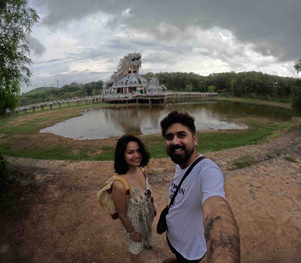 Two people posing with a lake behind and dragon statue