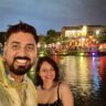 A man and woman standing at Hoi An Lantern Festival with background of water and lights