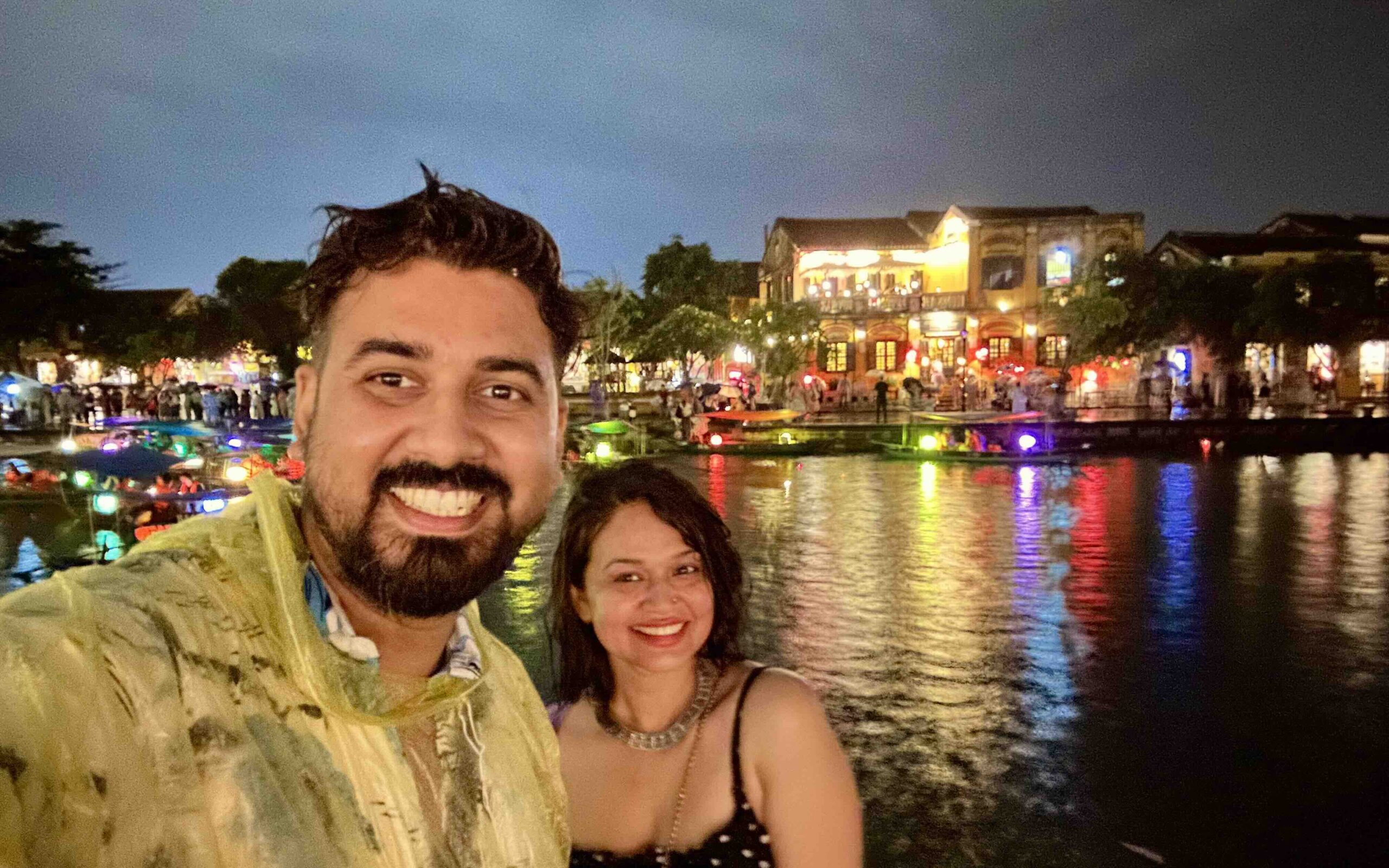 A man and woman standing at Hoi An Lantern Festival with background of water and lights