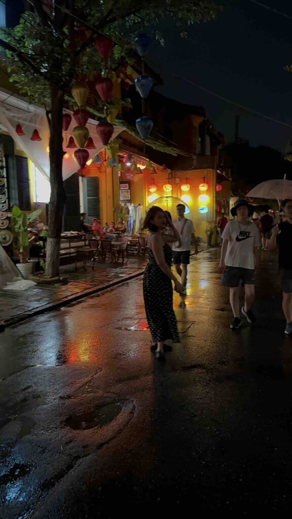 A person standing in rain with lanterns behind at Hoi An Lantern Festival