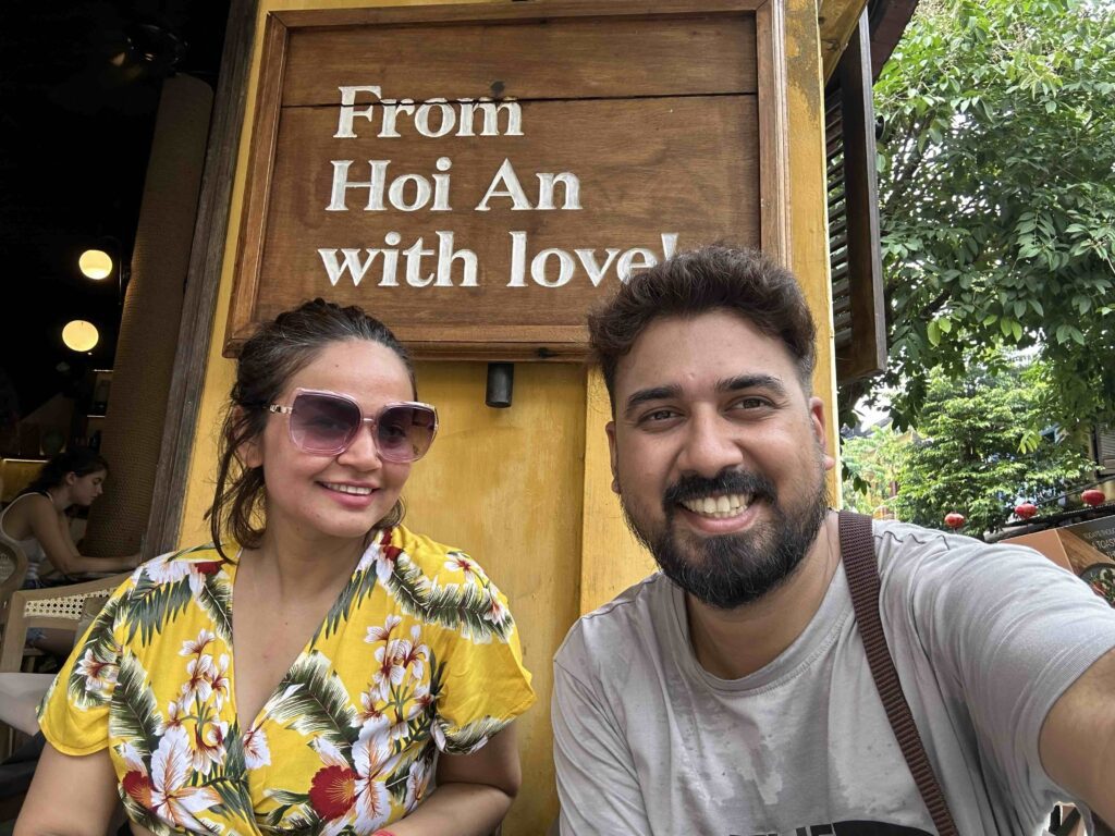 A man and woman posing in front of a board saying with love from Hoi An