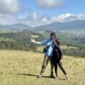 A man in a blue sweater and a woman in black clothes standing in an open grassland with mountains behind at Moon Plains, Nuwara Eliya Sri Lanka
