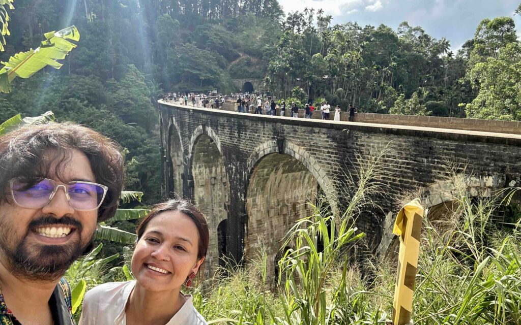 Two people looking at the camera and posing in front of Nine Arch Bridge in Ella Sri Lanka