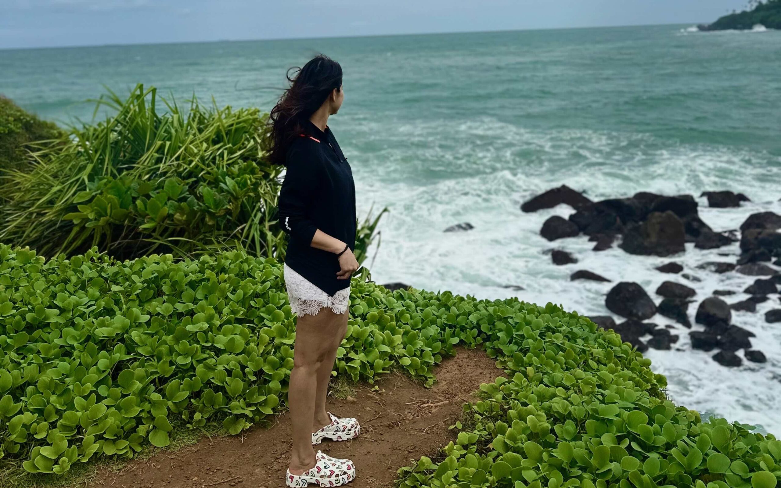 A person looking at the ocean standing on the cliff wearing a black jacket and white shorts at Parrot Rock in Mirrisa